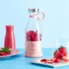 Portable electric bottle juicer with raspberries, fresh juice, and strawberries on a blue background