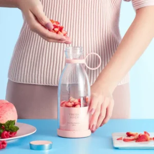 Woman preparing smoothie by adding strawberries to a pink portable electric juicer bottle