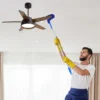 Man cleaning ceiling fan blades with flexible microfiber duster and telescopic handle